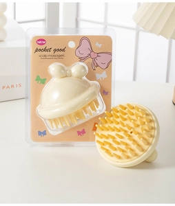 Close-up of a cream-colored scalp massager with a cute bow handle in retail packaging