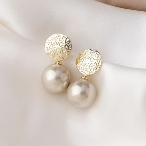 Detail of elegant gold C-shaped earrings with large faux pearls on a silk background