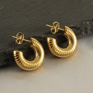 Détail macro de boucles d'oreilles dorées 18K à texture spirale sur pierre noire et soie