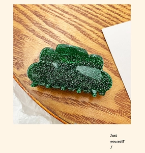 Detail of a medium green glitter hair claw clip with wave design on a wooden tray