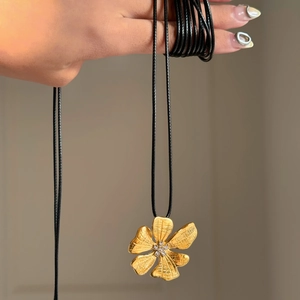 Macro shot of 18k gold flower pendant with small white rhinestones on black leather cord