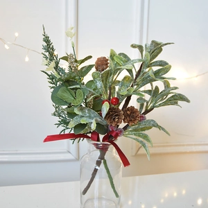 Christmas bouquet with pine cones, red berries, and cedar in glass vase on white background