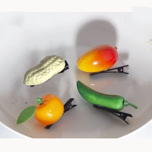 Detail of four creative food-shaped hair clips including peanut and mango in a white bowl