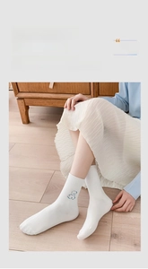 Detailed close-up of white cotton crew socks featuring blue bear embroidery and roll edge