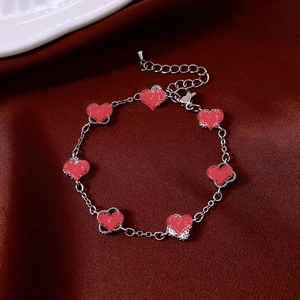 Detail of silver heart bracelet with red textured heart pendants on red silk background