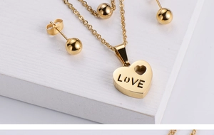 Macro detail of gold plated steel heart necklace with LOVE engraving and ball stud earrings