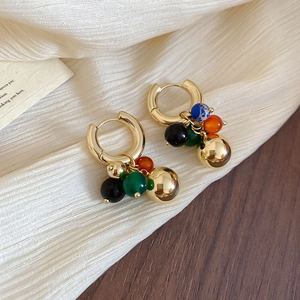 Macro view of gold hoop earrings with colorful beaded grape cluster pendants on silk fabric