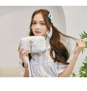 Close-up of white crossbody bag with embossed patterns and gold crown tassel detail