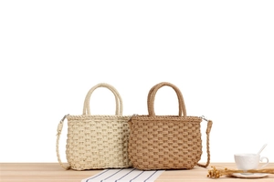 Detail of hand-woven paper straw bags in beige and brown on a rustic wooden table