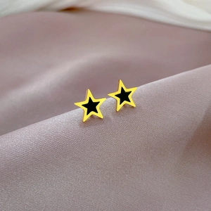 Macro detail of star-shaped stud earrings featuring golden edges and black center finish