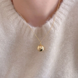 Minimalist gold round ball pendant necklace shown on a model wearing white knit sweater