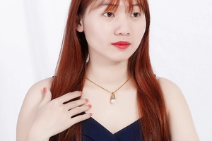 Detail view of an elegant gold necklace featuring a classic white pearl pendant on a model