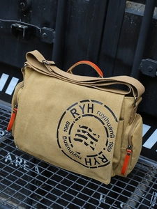 Sac messager en toile kaki avec poignées oranges sur grille métallique style industriel
