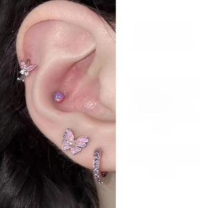 Close-up of pink butterfly ear bone studs and purple zircon earrings on female ear
