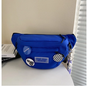 Detail of blue nylon chest bag with decorative pins and astronaut pendant on white table