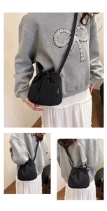 Detail of a casual black drawstring bucket bag showing adjustable shoulder strap and nylon fabric