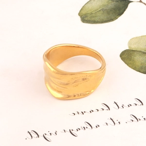 Detail view of a gold wavy irregular ring with natural textures on a warm white background