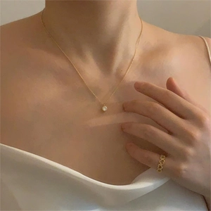 Close-up of minimalist gold zircon pendant necklace and heart-shaped ring on a model