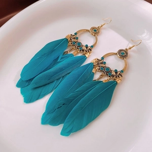 Détail de boucles d'oreilles bohèmes avec fleurs et plumes bleu paon sur plateau blanc