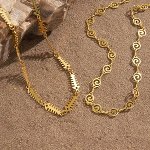 Bohemian gold fishbone and spiral link necklaces displayed on beach sand and rock