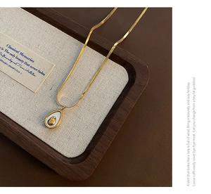 Detailed close-up of golden teardrop shell pendant on a snake bone chain in a tray