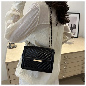Model wearing a black quilted crossbody bag with gold chain strap in a stylish interior
