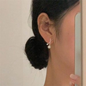 Detail of elegant silver pearl cross earrings worn by a model in a minimalist style