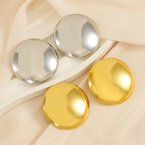 Detail of round gold and silver stainless steel stud earrings on beige silk fabric
