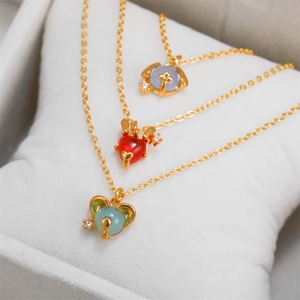 Close-up of three 18K gold animal pendants with colorful stones on a white cushion