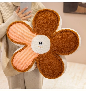 Close-up of a cozy smiling flower-shaped plush pillow held in a warm home interior