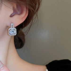 Detailed close-up of square zircon halo earrings worn by a model in warm lighting