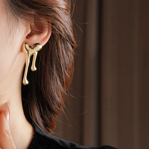 Close-up of a model wearing a gold metallic heart earring with a fluid-melt design
