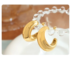 Macro view of polished 18k gold plated chunky C-shaped hoop earrings with stud back