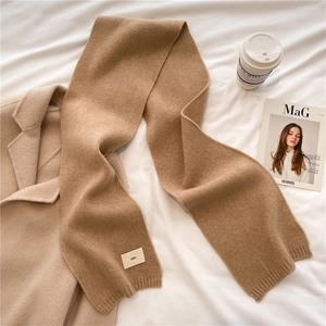 Flat lay of soft camel knitted scarf with emo label on white sheet with coffee