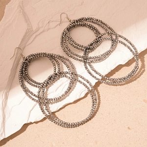 Close-up of layered interlocking dark grey bead hoop earrings on white plaster stone