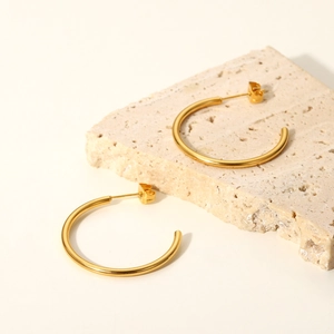 Polished 18K gold stainless steel C-shaped earrings on a beige natural stone base