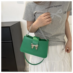 Detail of green shoulder bag with silver bow ornament and chain strap held by model