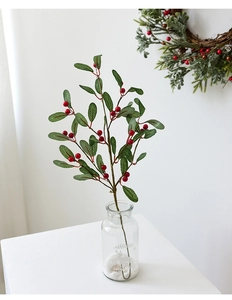 Detail of festive artificial red berry and pine branch in a glass vase with reindeer motif