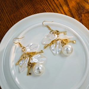 Detail shot of vintage flower pearl earrings with golden key charm on white ceramic plate