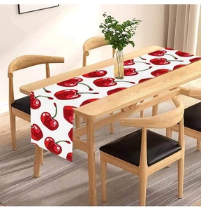 Detailed close-up of a linen table runner with red cherry print on a wooden dining table