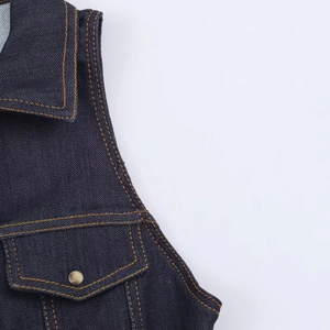 Close-up of dark blue denim jumpsuit with metal button pocket and contrast yellow stitching