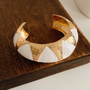 Detailed macro view of vintage gold and white enamel bangle on a wooden stand