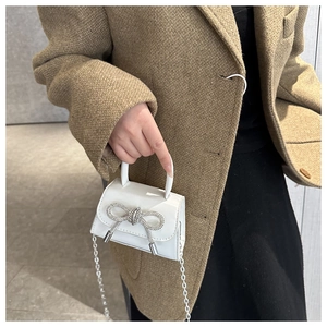 Close-up of mini white patent leather crossbody bag with silver rhinestone bow detail