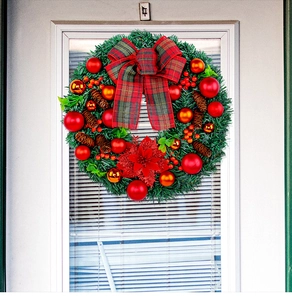Close-up of Christmas wreath with red bow, golden baubles, and pine cones on a white door