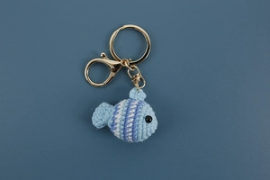 Detailed view of handmade crochet blue fish keychain with golden lobster clasp on blue background