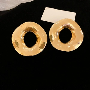 Détail de boucles d'oreilles anneaux dorés irréguliers avec texture froissée sur velours