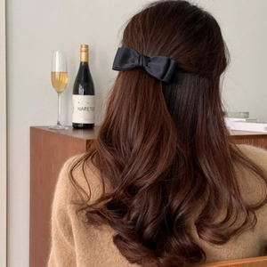 Elegant black satin bow hair clip styled in a half-updo on dark wavy hair for women