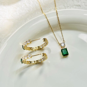 Detail of emerald green rectangular stone necklace and C-shaped earrings in gold finish
