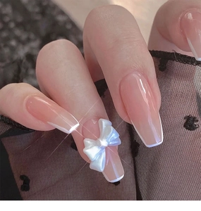 Close-up of long trapezoid French nails featuring a 3D white pearl bow and pink base