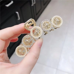 Close-up of golden hair claw clip featuring starburst patterns and pearl accents